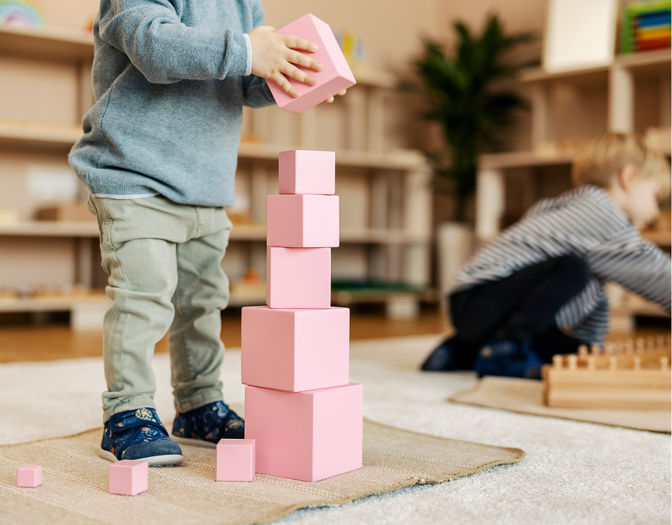 Child stacking pink blocks in classroom.