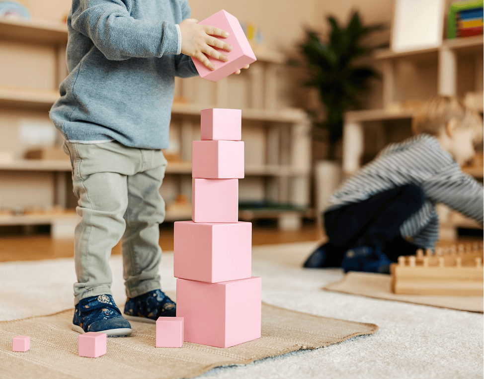 Child stacking pink blocks in classroom.